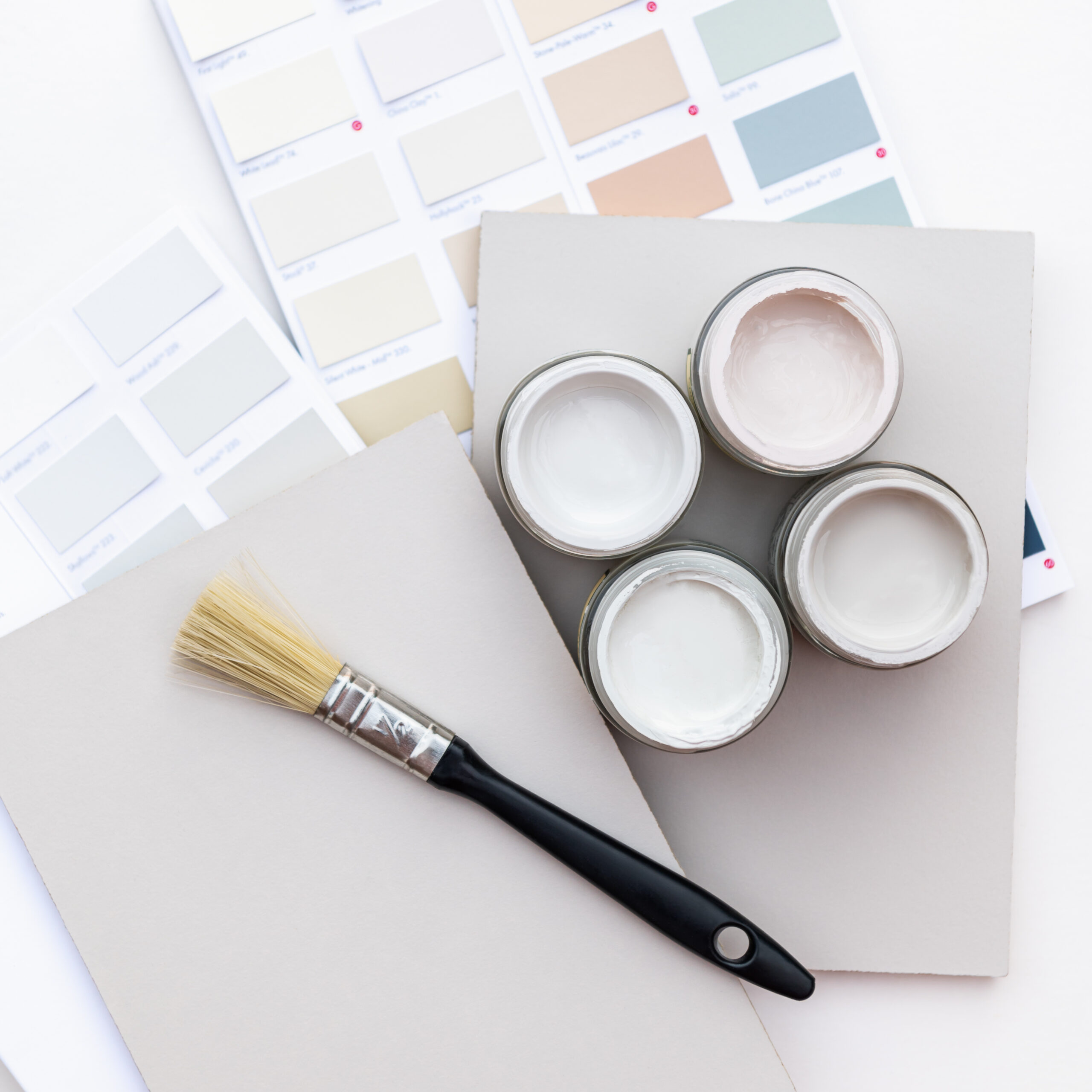 Tiny sample paint cans during house renovation, process of choosing paint for the walls, light grey and pastel colors, color charts and unit samples on background