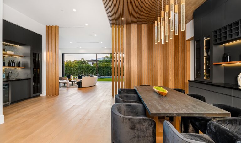 Modern open-plan dining and living area with wooden accents, contemporary furniture, and large windows overlooking a garden.